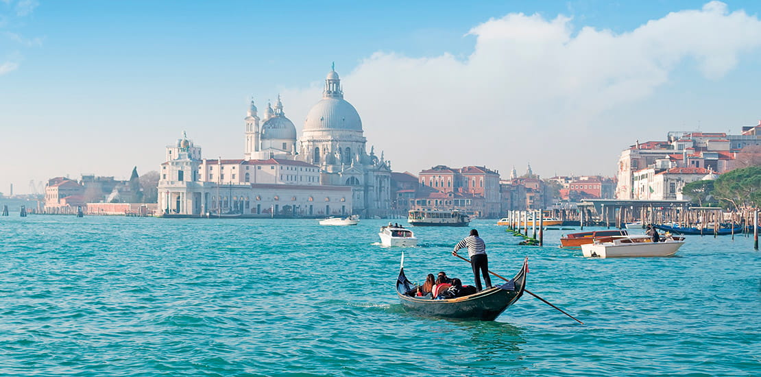 People in a gondola on the canals of Venice, with Santa Maria della Salute in the background, Italy.